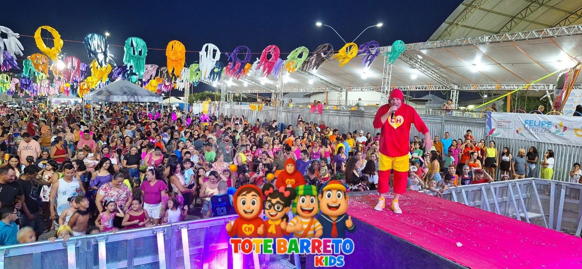 Tote Barreto no palco do carnaval, praça decorada com sombrinhas coloridas e multidão